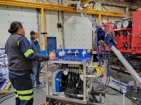 A Multi-Power Products Ltd employee (foreground) demonstrates the BASE Drill to IDP engineer/driller Elliot Moravec (background). Credit: Jay Johnson.